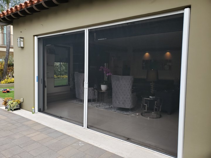 White-framed retractable screens across a wide living-room opening, viewed from outside