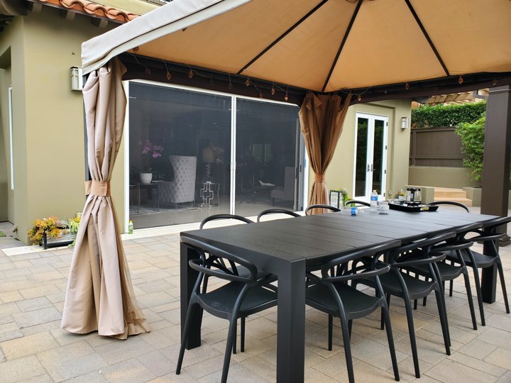 Wide white-framed retractable screens viewed beyond an outdoor dining table under a canopy